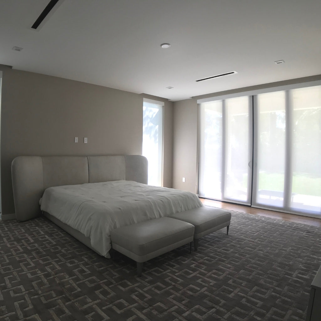 light bedroom with a white bed in the middle. Windows are closed with shades.