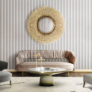 big round mirror in a golden frame that looks like a sun. Silk pink couch and striped wallpaper