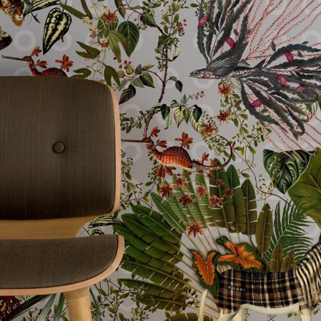 Animal print wallpaper showing extinct animals. Wallpaper has green banana leaves, colorful orange accents and tones of pink and green. There is a wooden style chair in front of the wall.