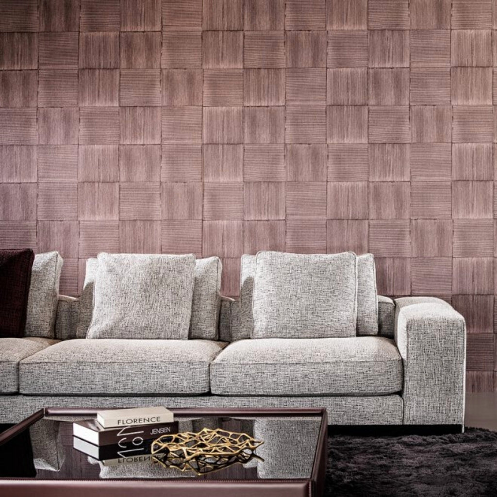 pink textured wallpaper with many squares. A gay big couch in front of the wall and a mirror table with a violet frame. Travel books on a table. 